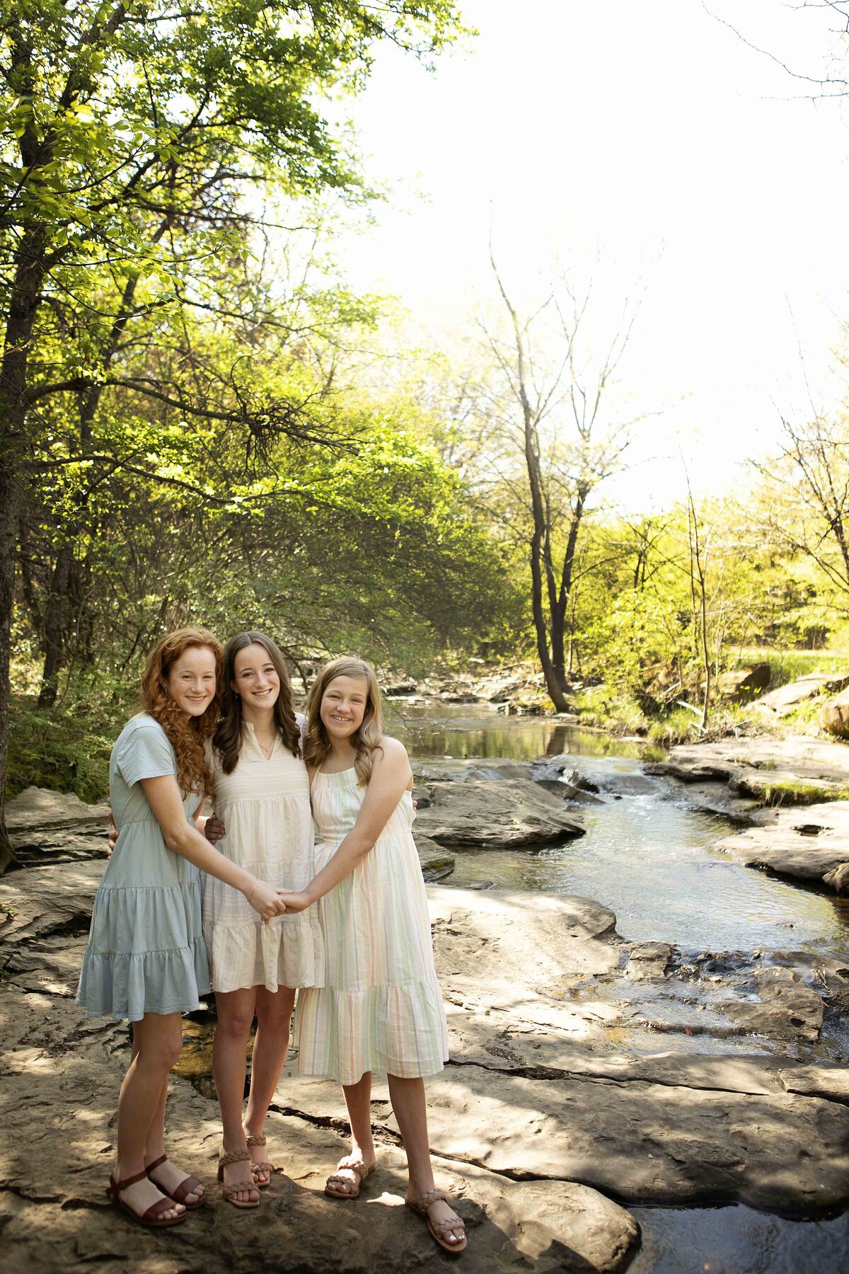 Sisters standing on the creek bank in Flower Mound, with wildflowers surrounding them as they strike a joyful pose