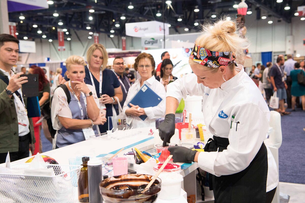 Female chef demonstrates how to make chocolate syrup attendees at expo