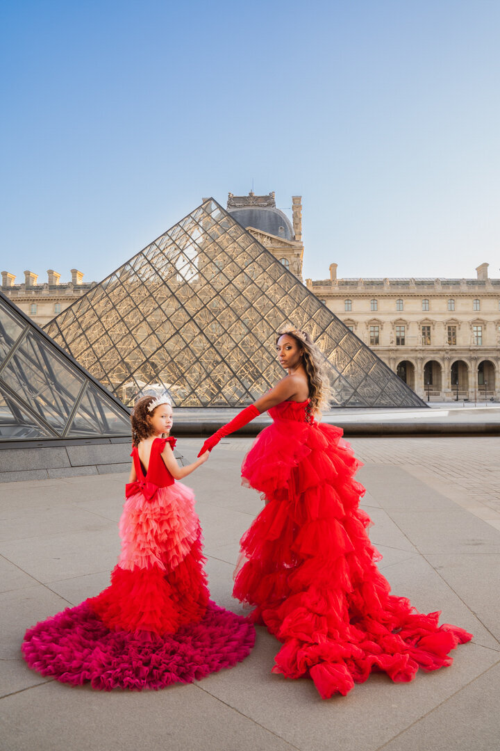 Elegant mother-daughter portrait at the Louvre pyramids with matching crowns and princess dresses