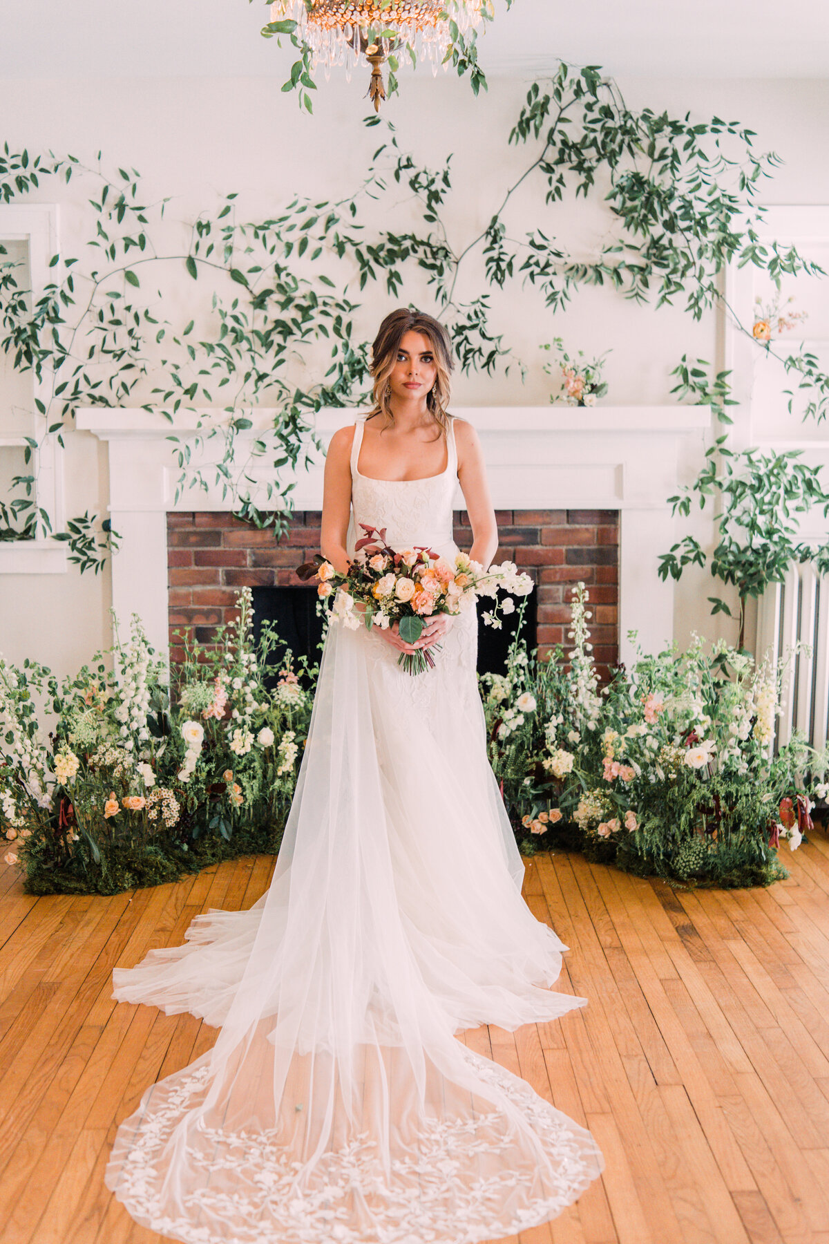 Bride wearing Alexandra Grecco Marcelle gown & Ainsley veil holding bouquet before vine-covered mantle & garden ceremony nest