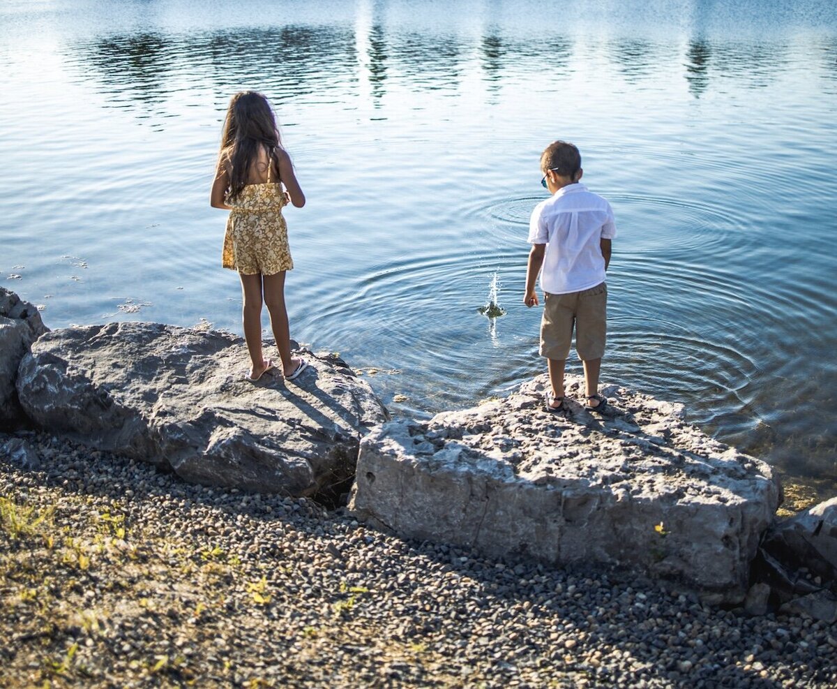A little girl and little boy standing on large rocks overlooking a lake