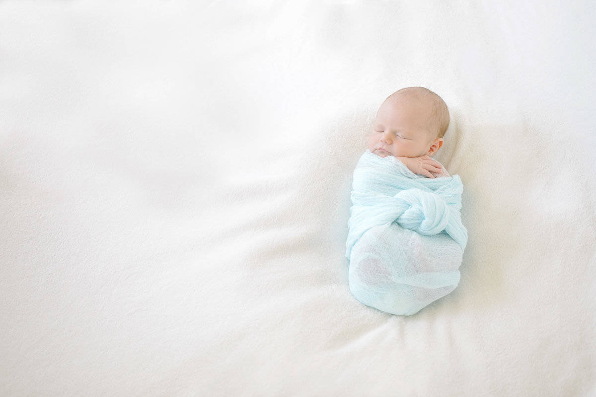 baby swaddled in light blue wrap on white blanket