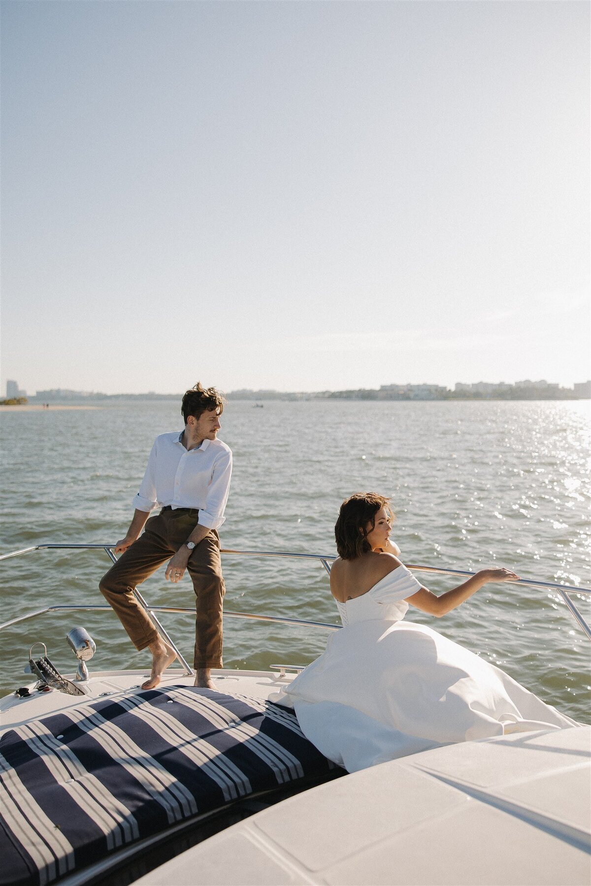 Bride and groom sit on stern of yacht, looking out over the shimmering water.