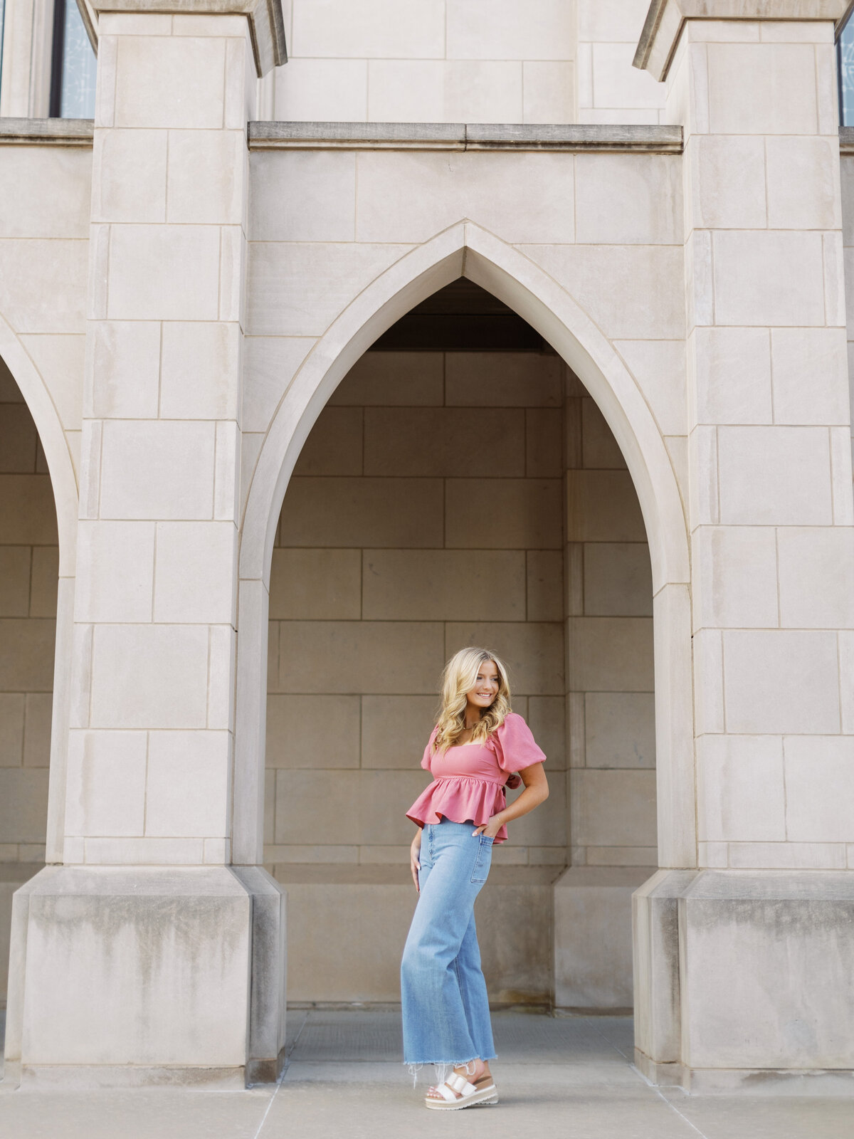 Young woman poses confidently in front of tulsa archway for senior photos