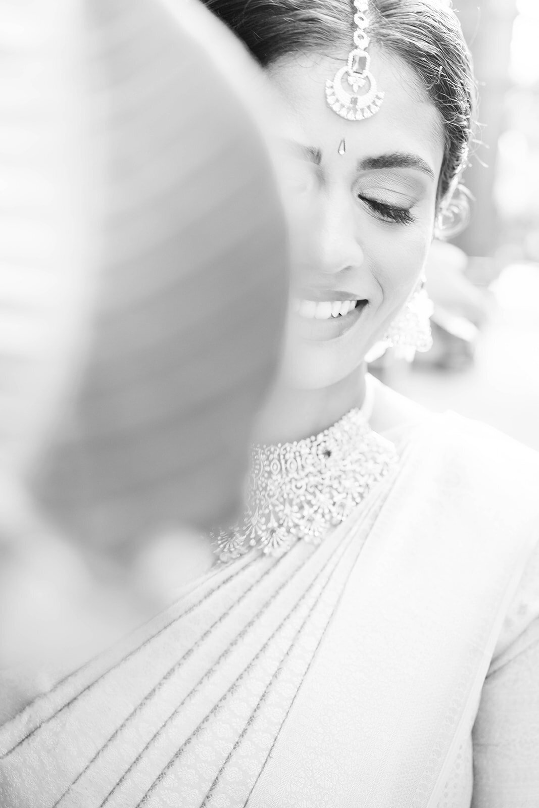 Close-up black and white portrait of a South Asian bride smiling softly in a traditional saree, captured during a wedding at The Mayflower Hotel in Washington DC by Mari Harsan Studios.
