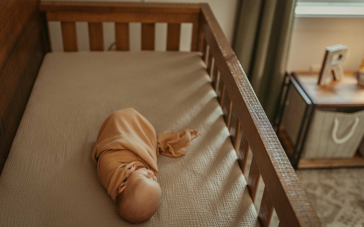 baby wrapped in tan blanket sleeping in his wood crib