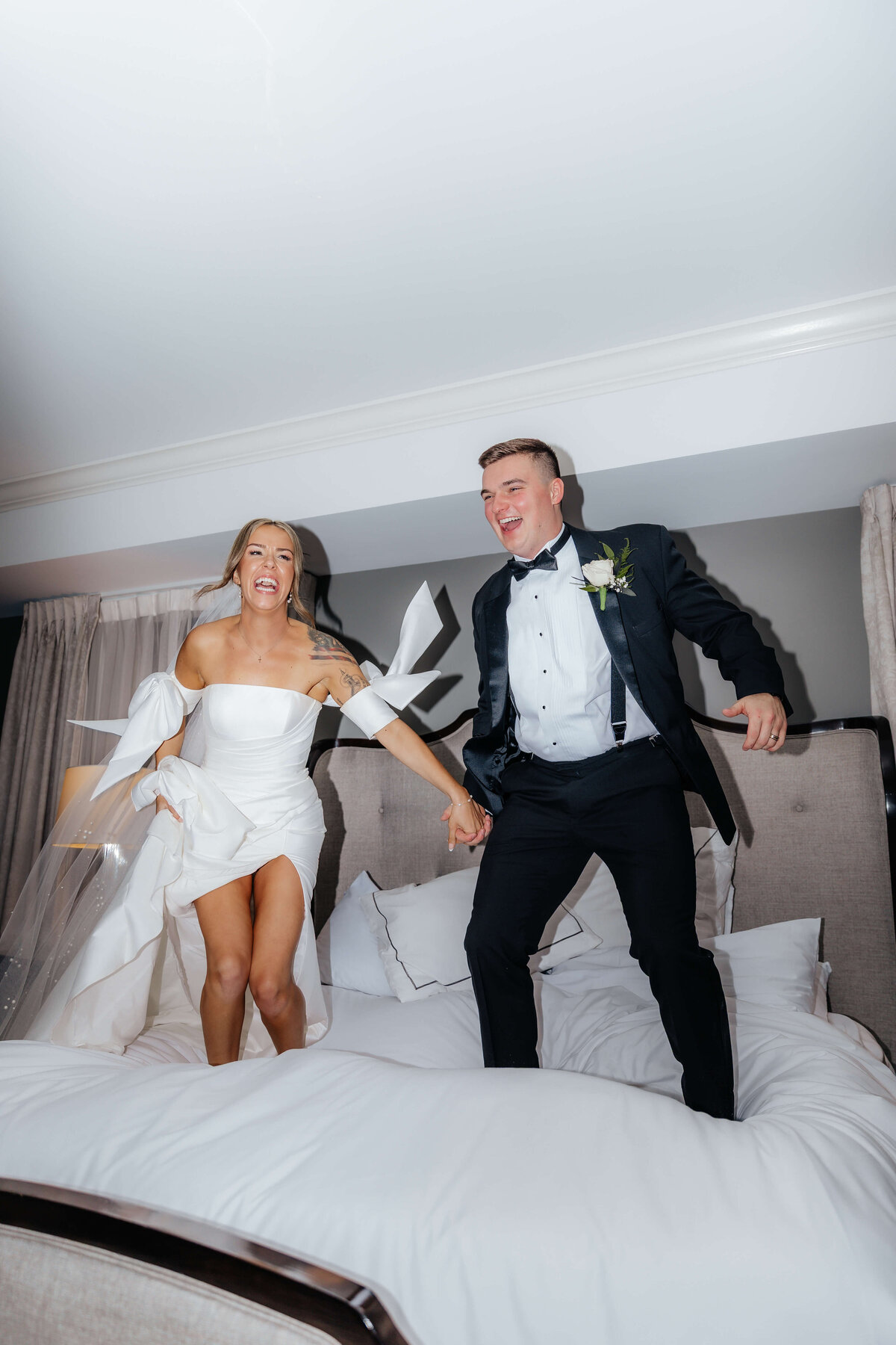 Bride and groom jumping on bed in wedding attire, playful and unposed Ohio wedding photography for couples who crave candid, fun storytelling