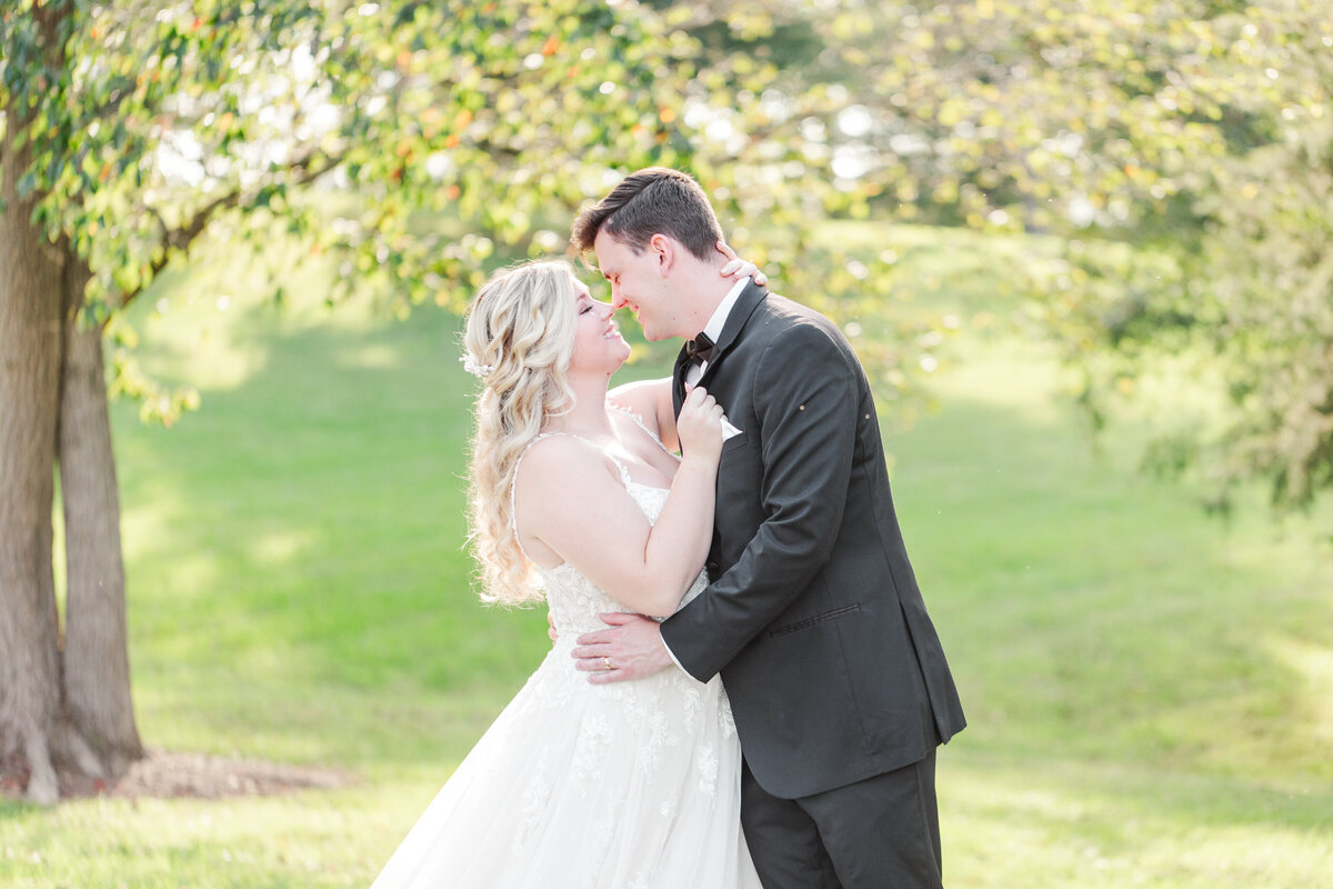 Happy bride and groom rubbing noses together under bright, summer trees taken by Jennifer & Daniel Cooke, local Nashville wedding photographers.