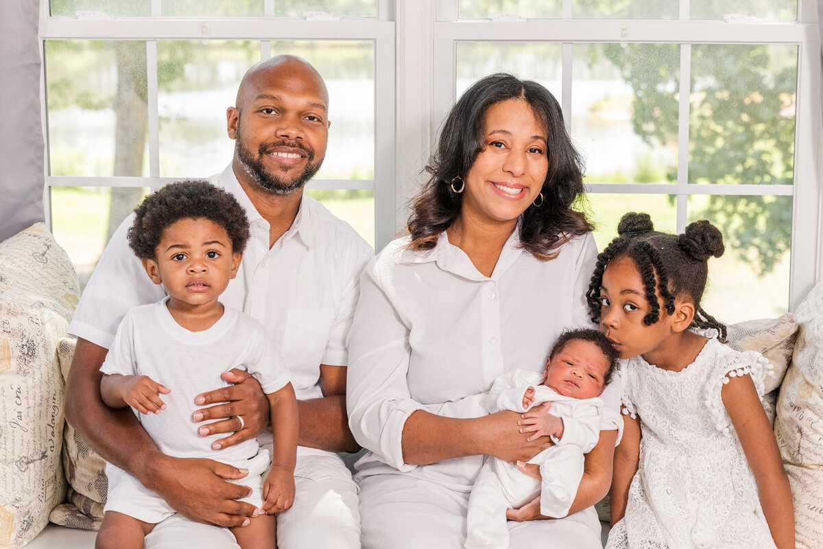 family of 5 wearing white outfits and sitting in front of a window with 2 toddlers and a newborn baby boy Laure Photography Atlanta family and newborn photographer