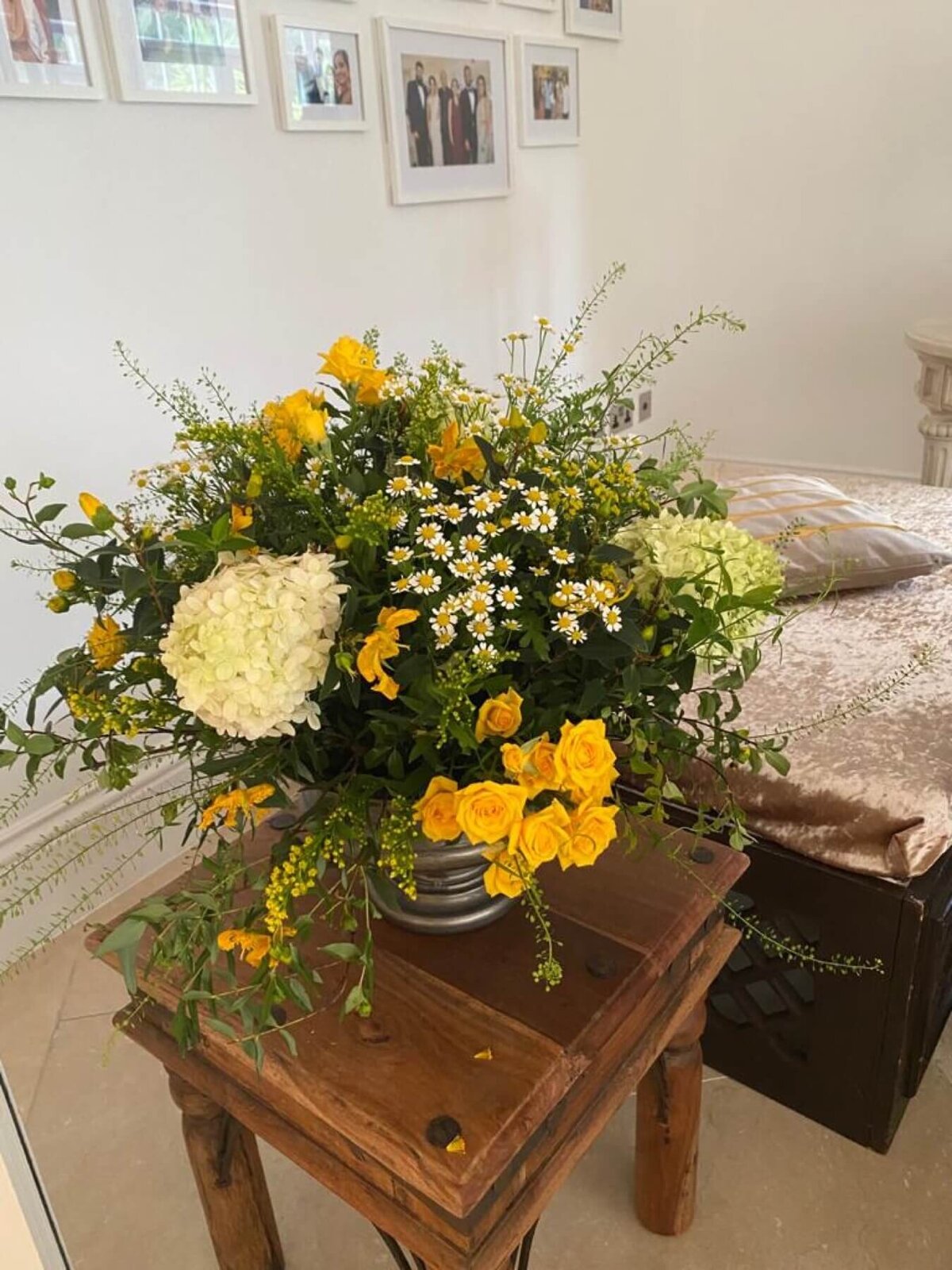 Large yellow flower arrangement on a wooden table filled with daisies, roses and hydrangeas