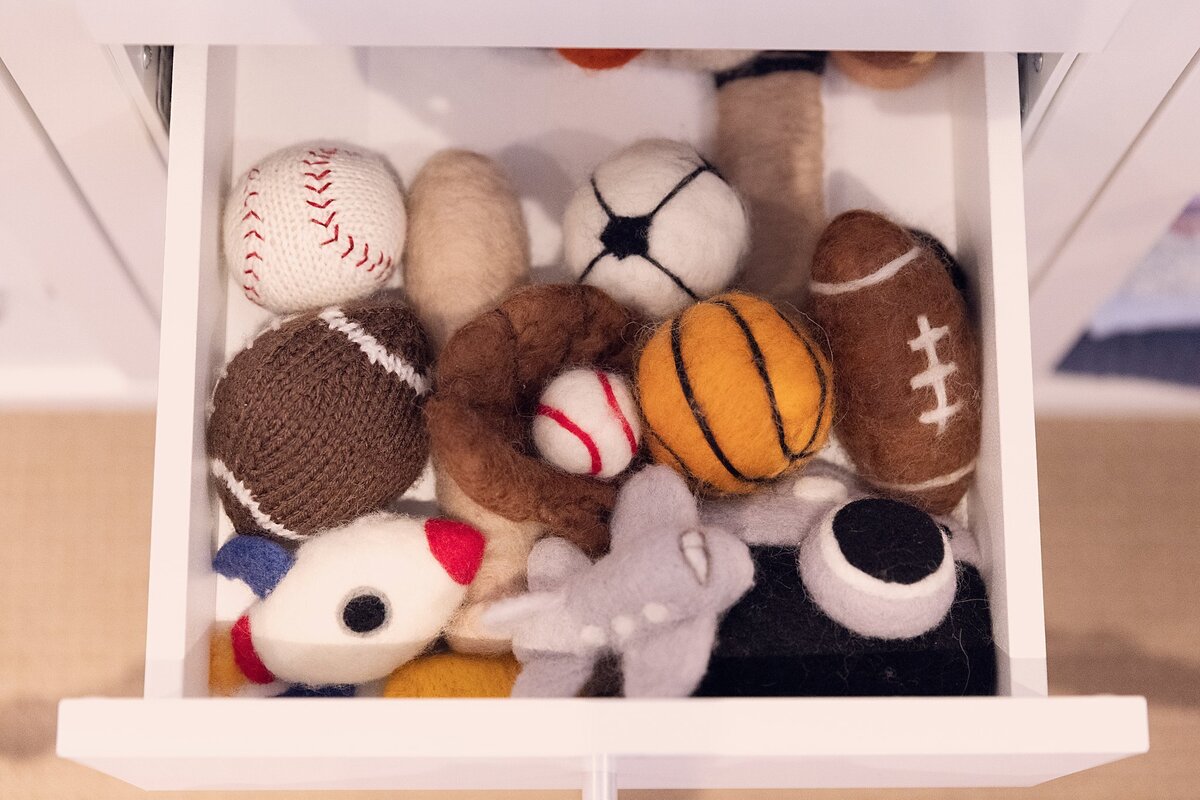 Drawer containing sports-themed newborn photography props, including knit baseballs, basketballs, hockey pucks, and footballs.