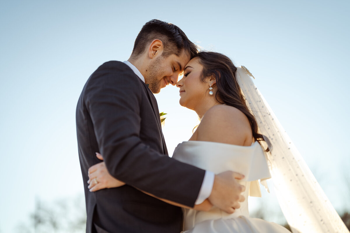 Romantic close-up of a bride and groom sharing an intimate embrace, foreheads touching as they smile softly during their winter wedding at D'Vine Grace Vineyard. The gentle sunset light adds warmth and love to the moment.