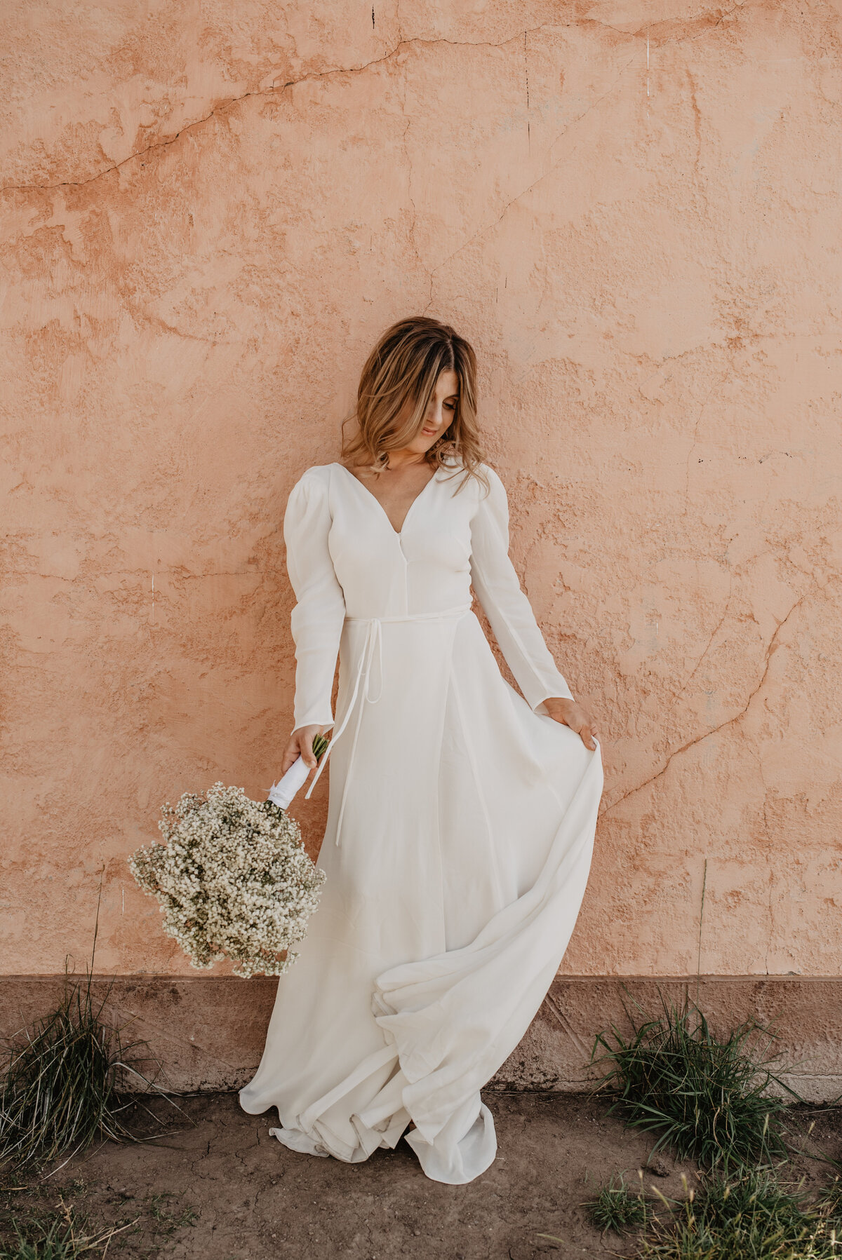 bridal portraits by jackson wyoming photographer with bride standing in front of a clay buildin gin jackson hole holding her wedding dress out to the side