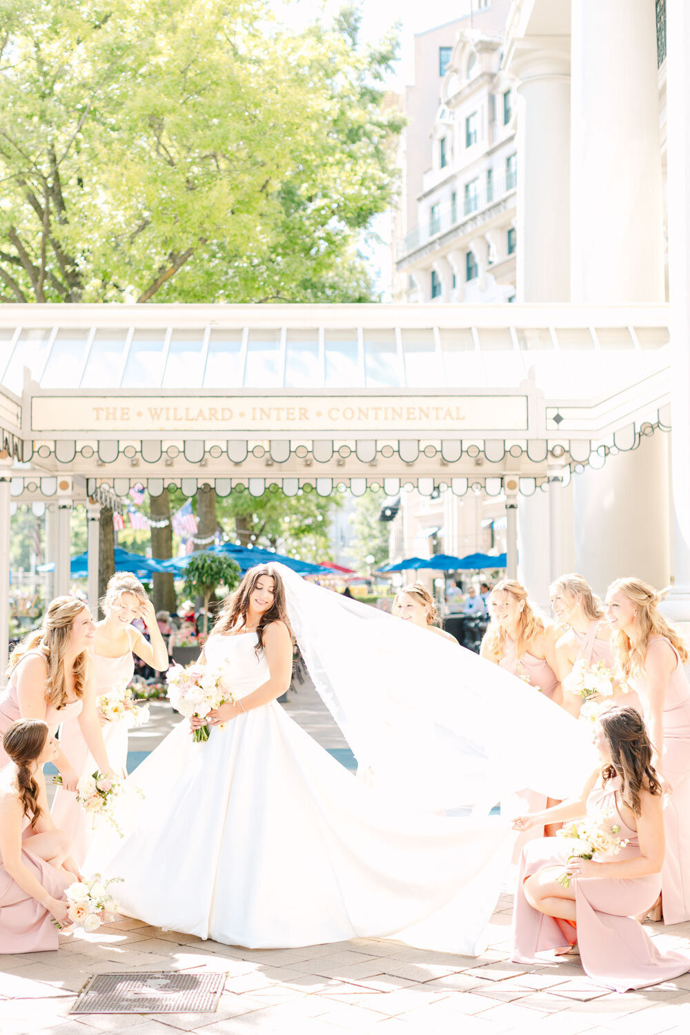 Bride tossing veil outside hotel with bridesmaids.