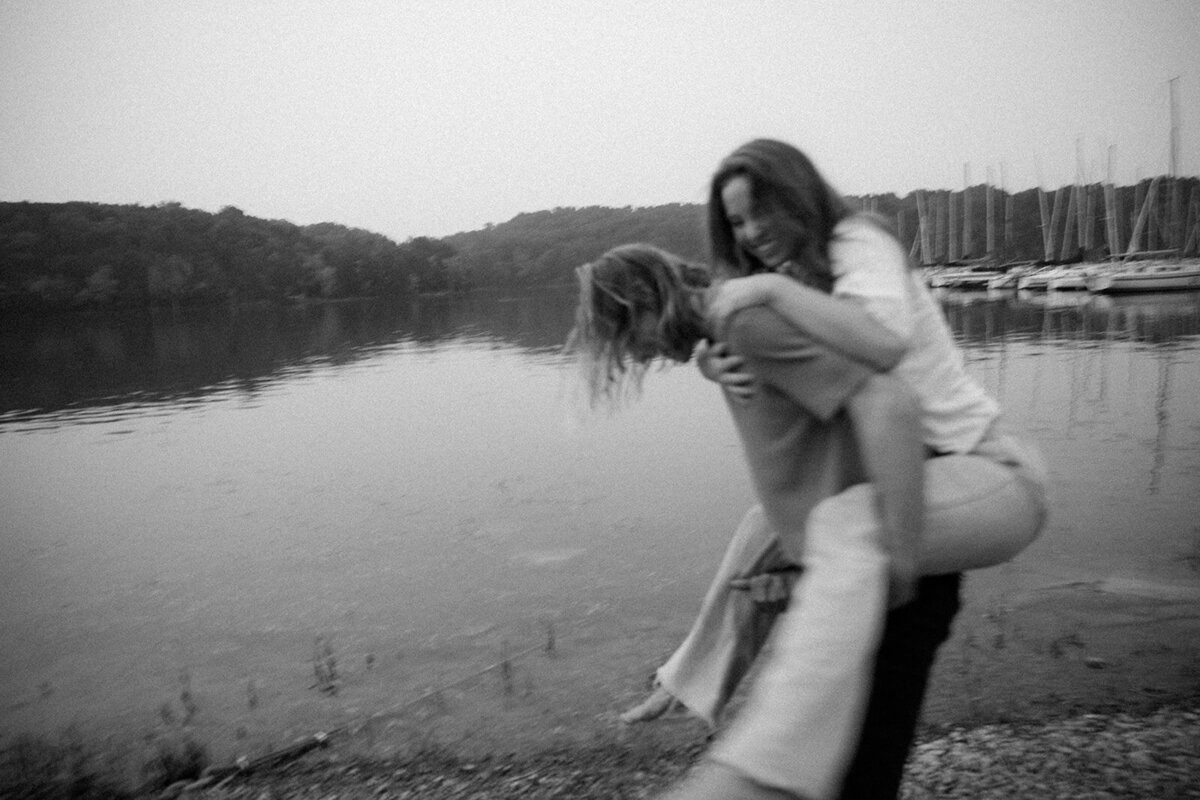 Man gives woman playful piggy back ride on lakes edge during romantic couples session. 