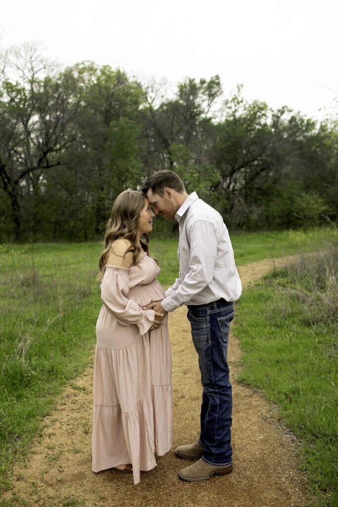A beautiful maternity photo of the husband and wife in the park, sharing a quiet moment as they stand close, with the wife gently cradling her belly while the husband wraps his arm around her, captured by Chunky Monkey Photography.