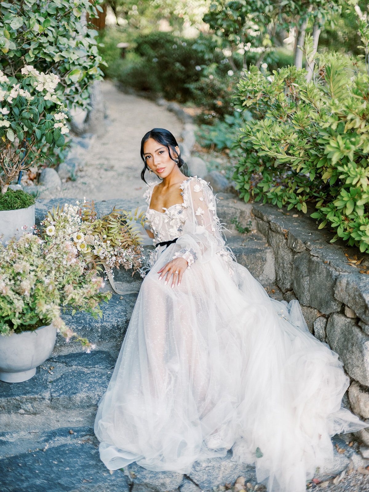 Gorgeous bride wearing a long sleeve wedding gown, sitting on the steps at a luxury vineyard in Paso Robles, California for her wedding day