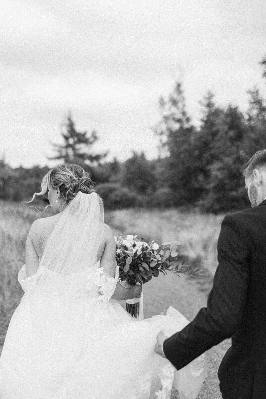 Groom-holds-brides-dress-as-they-walk