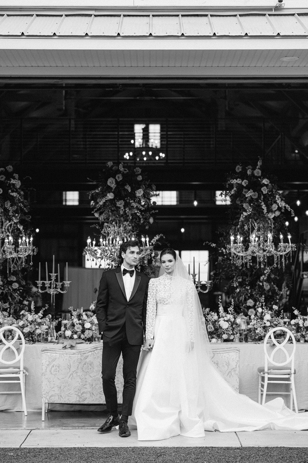 Black and white photo of bride and groom posing in front of decorated tables at Groom in a pink jacket and bride in an elegant dress posing for a portrait at Wildflower On Watts