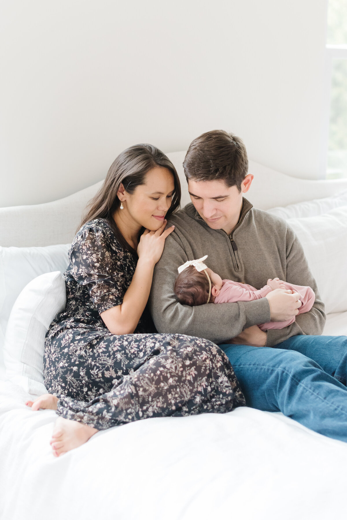 Mom and dad sitting on bed holding newborn and looking down  - Northern Virginia Newborn Photographer
