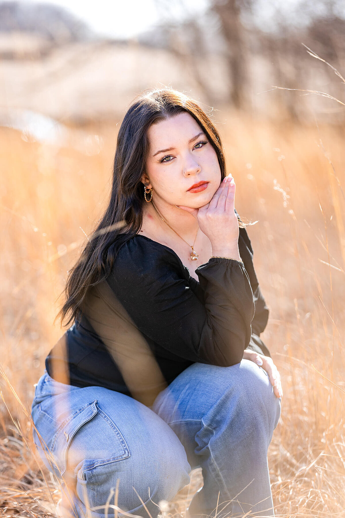 Beautiful senior girl poses in tall grasses during her photo session.