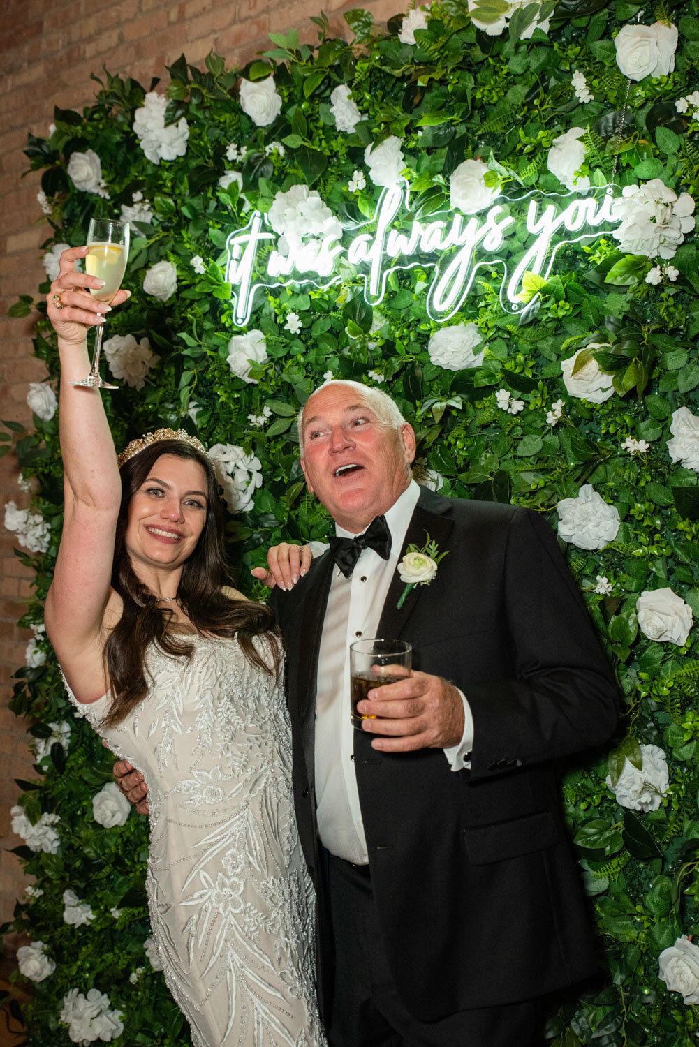 A bride and groom toasting in front of a sign that says i love always you