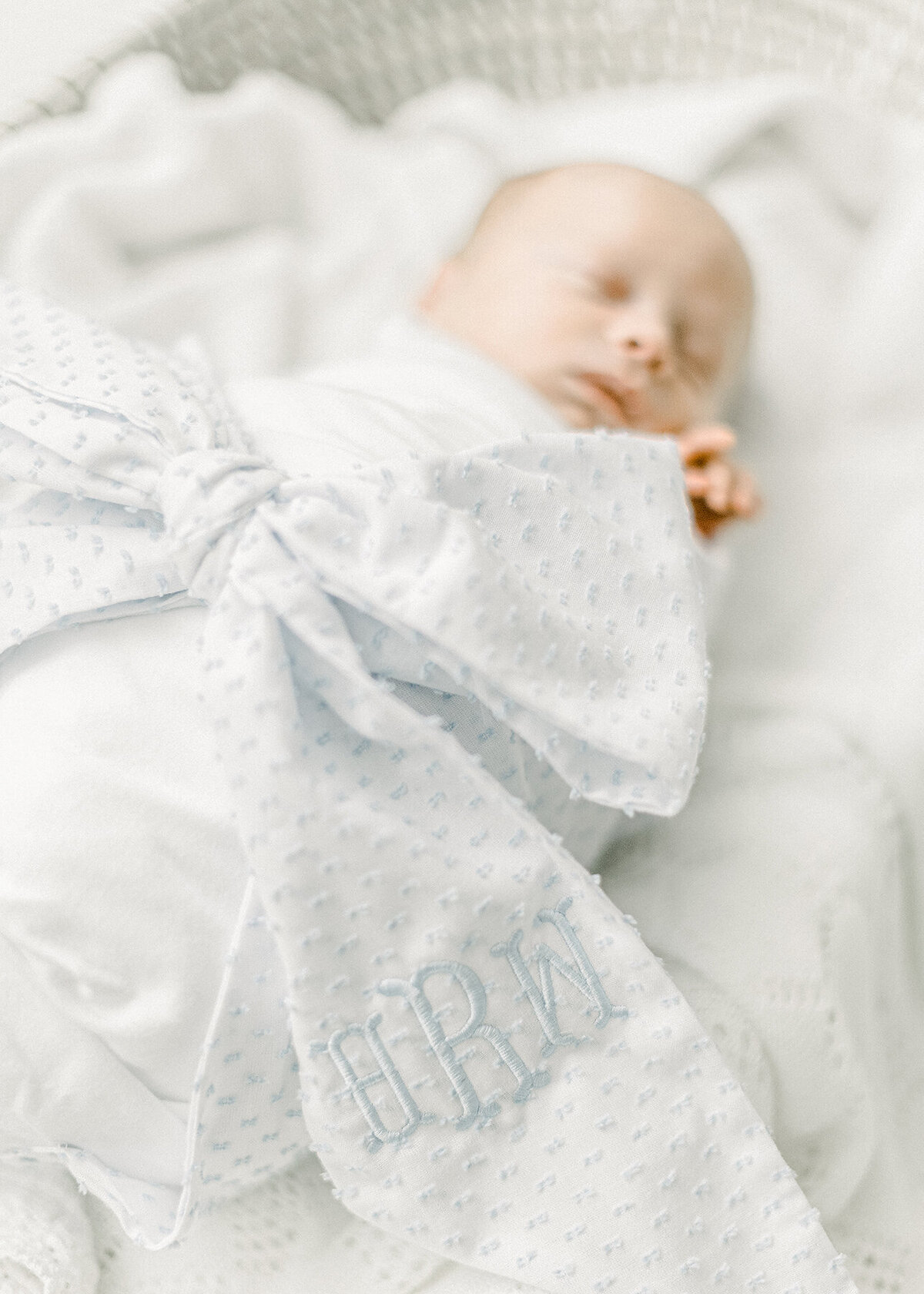 Newborn baby boy laying in a basket swaddled and tied with a light blue bow as he sleeps in a basket on the floor of a DFW photography studio.