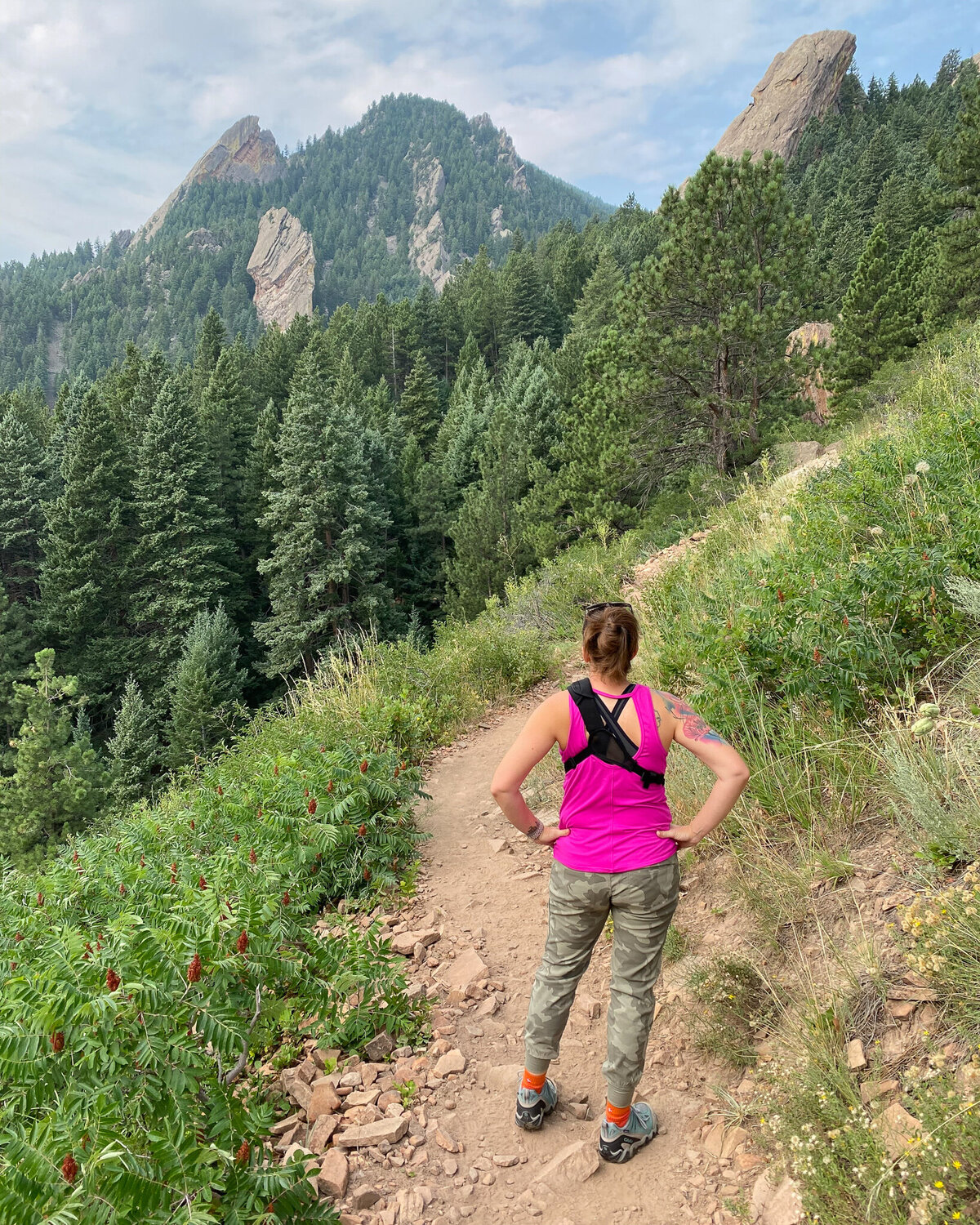 woman standing on a hiking path looking at the mountains in front of her, wearing hiking gear