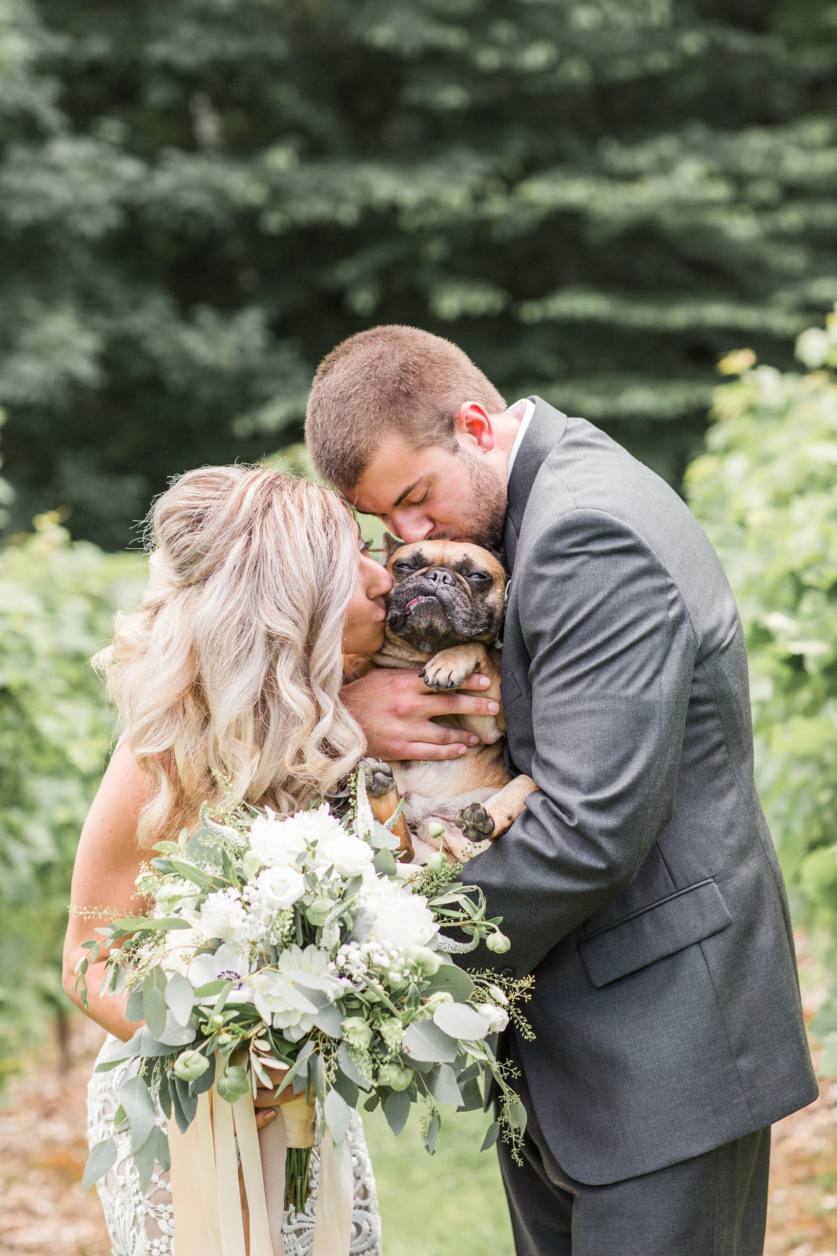 Bride and groom kissing their French Bulldog in a winery