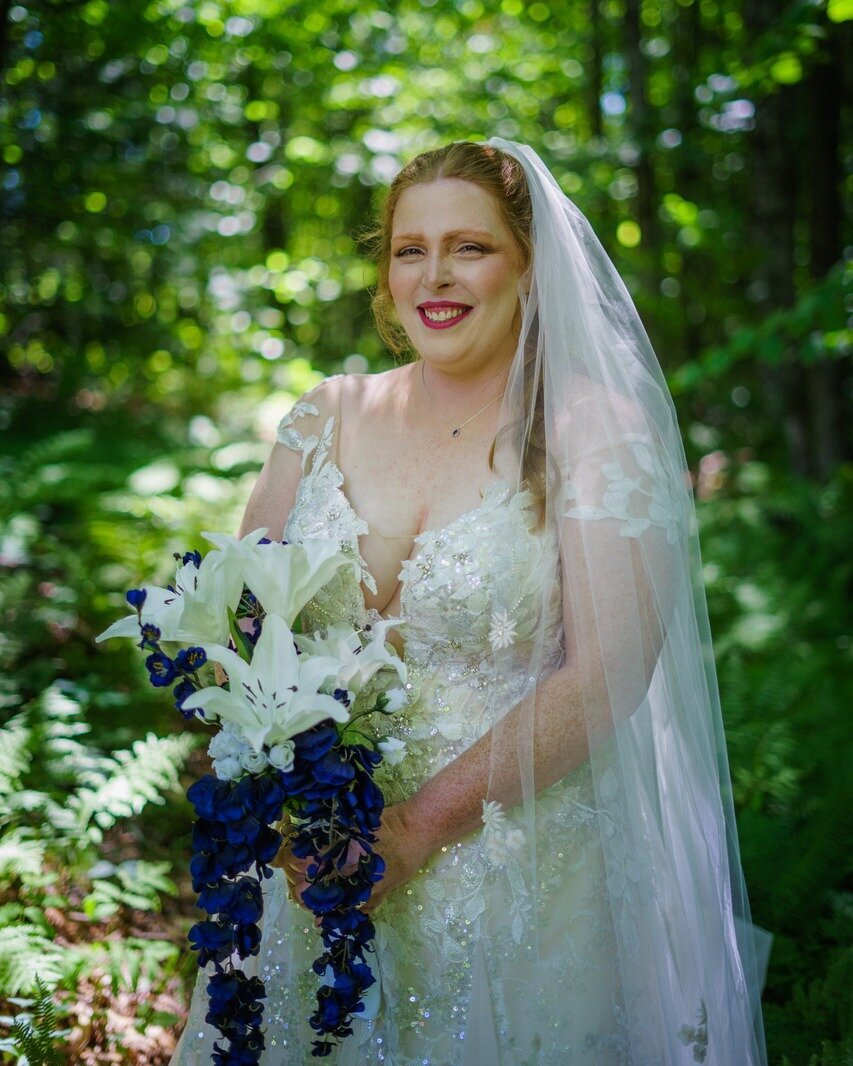 a bride in the woods with white and blue flowers