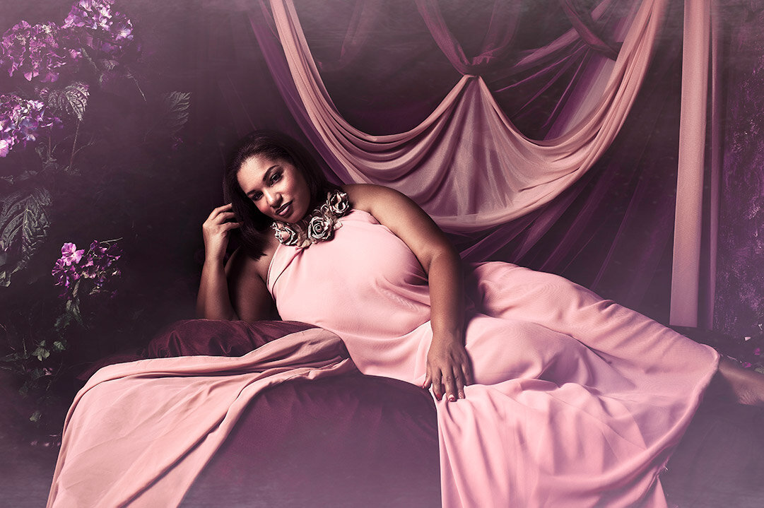 A painterly boudoir image of a woman draped in pink fabric in a Grecian setting.