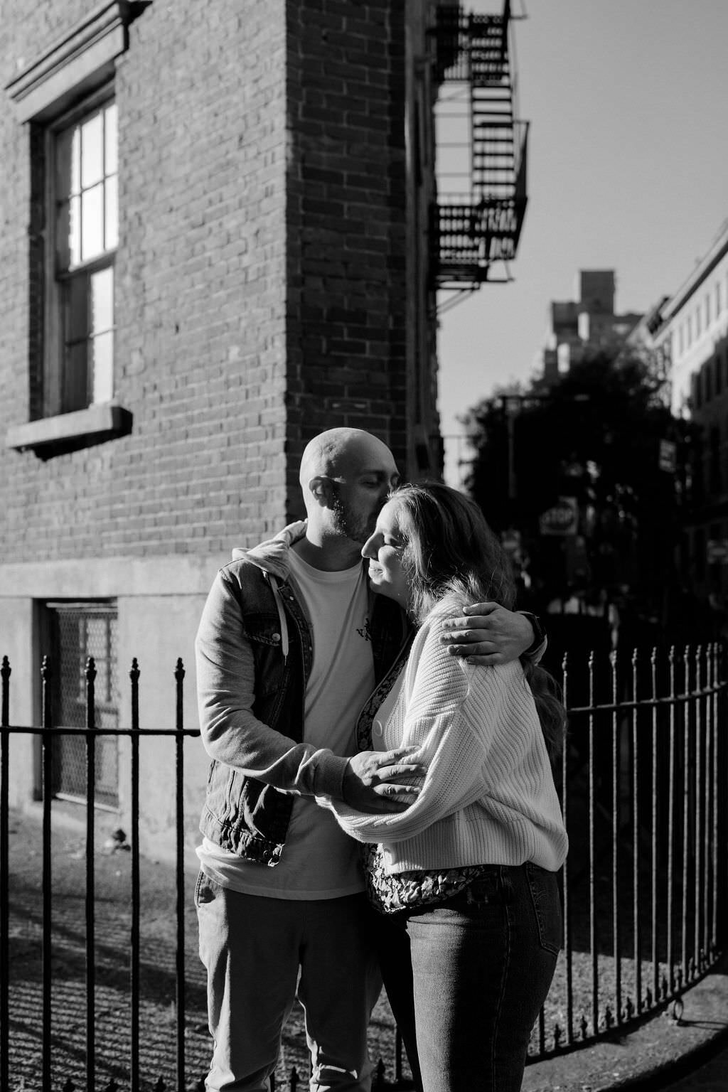 man hugging woman and kissing her head as they stand on the corner of a street
