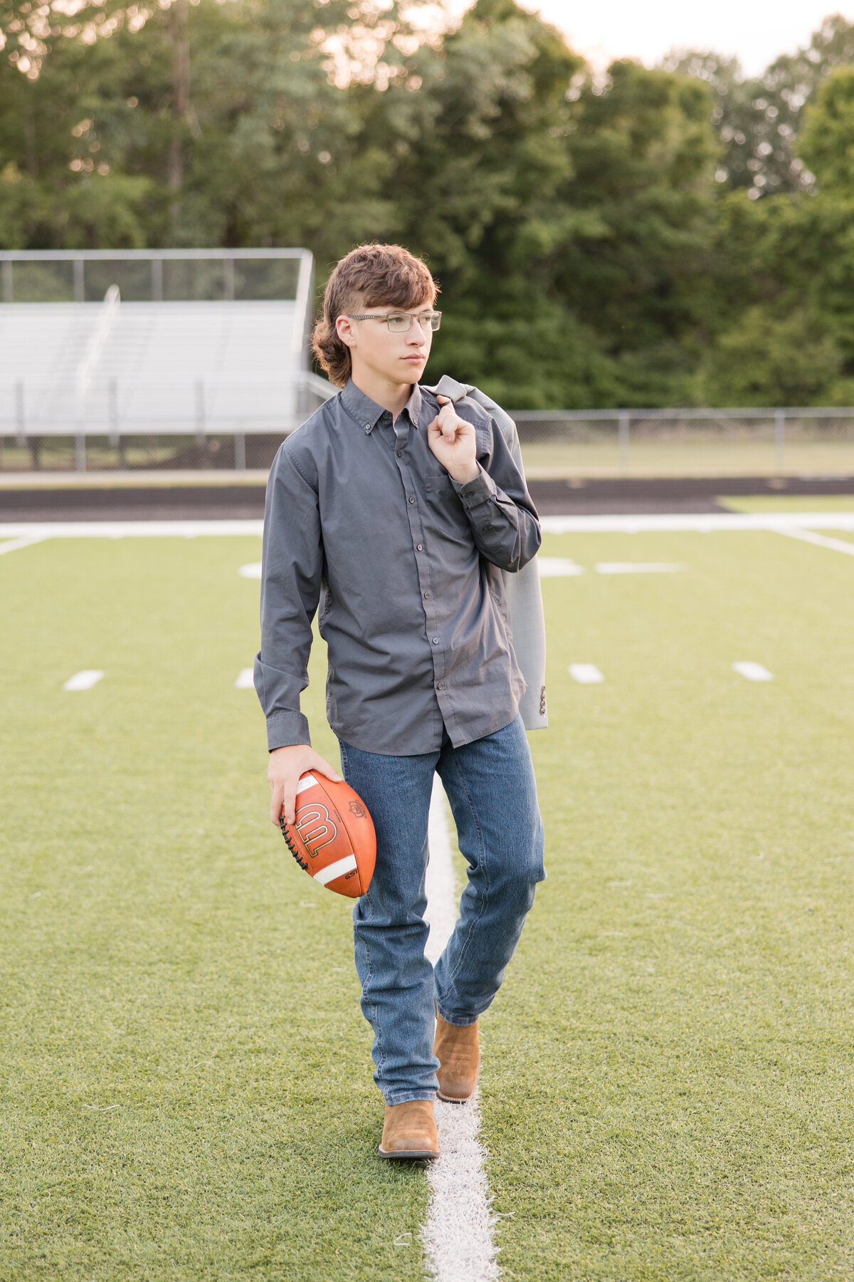 Senior guy standing in a football field holding a football and looking away
