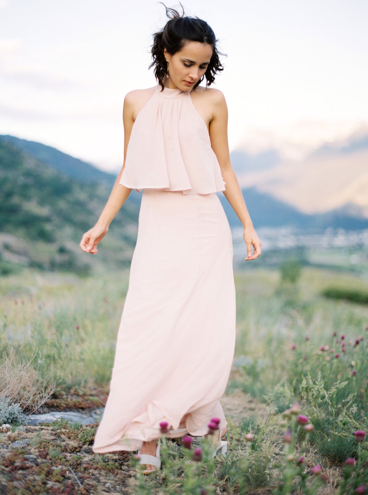 Woman walks through wildflower filled field in pink chiffon dress