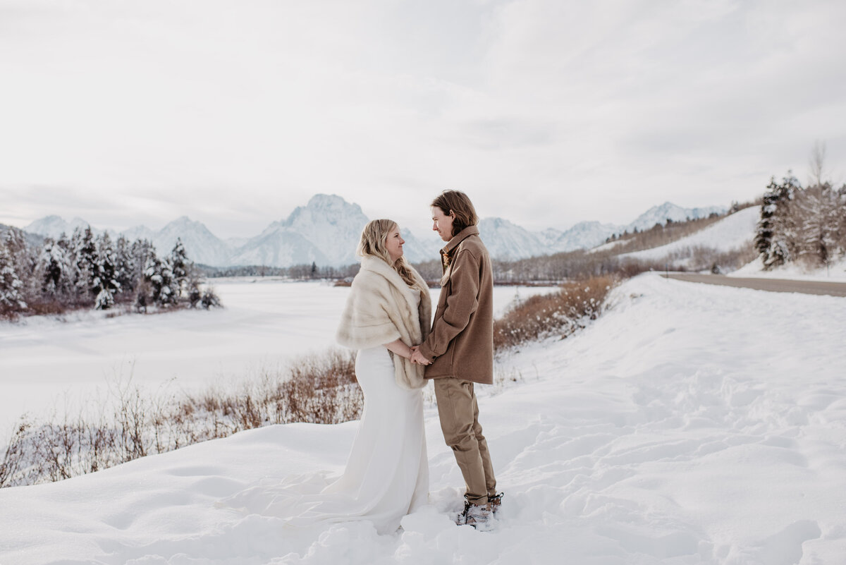 winter wedding in the Grand Tetons with brie and groom standing on a stream and holding hands as they face one another