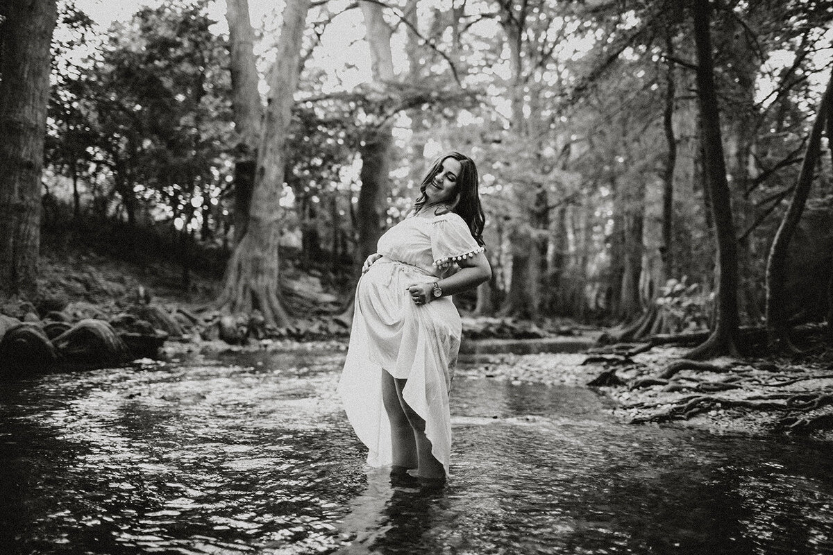 Black and white maternity portrait of a pregnant woman standing in a river, photographed by San Antonio family photographer Sara James.