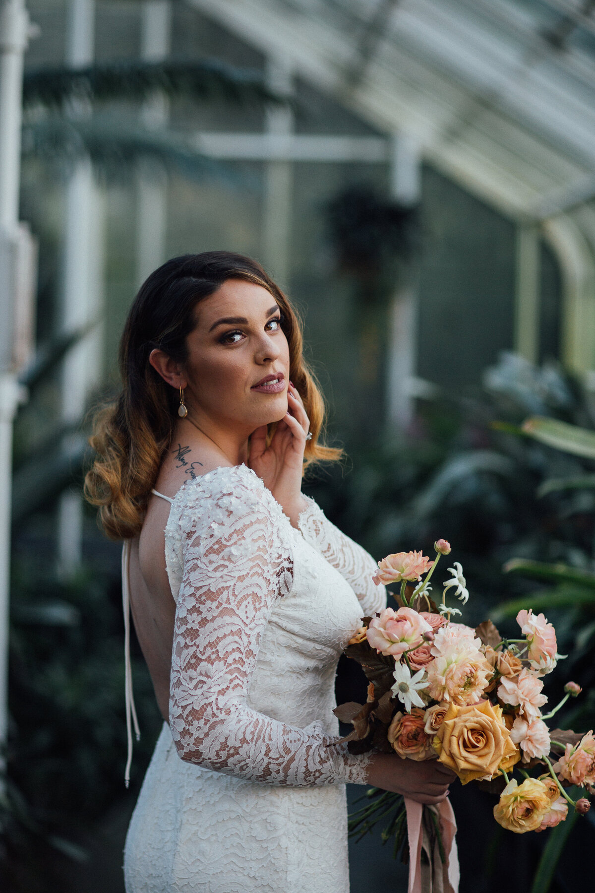 This all-lace wedding dress has a crepe underlayer except for under the long sleeves which are sheer. The shoulders of the sleeves are adorned with small 3D flowers and crystals and the cuff is finished with a lace scallop edge.