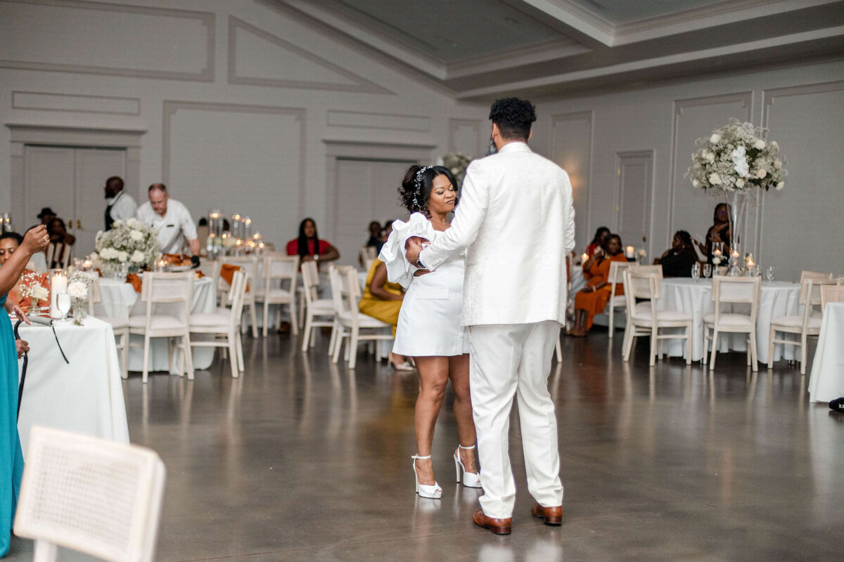 Newlyweds sharing a joyful dance, surrounded by guests in a modern reception space.