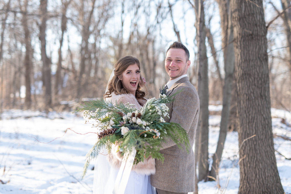 Bride and groom embrace while holding lush bouquet outdoors in the snow