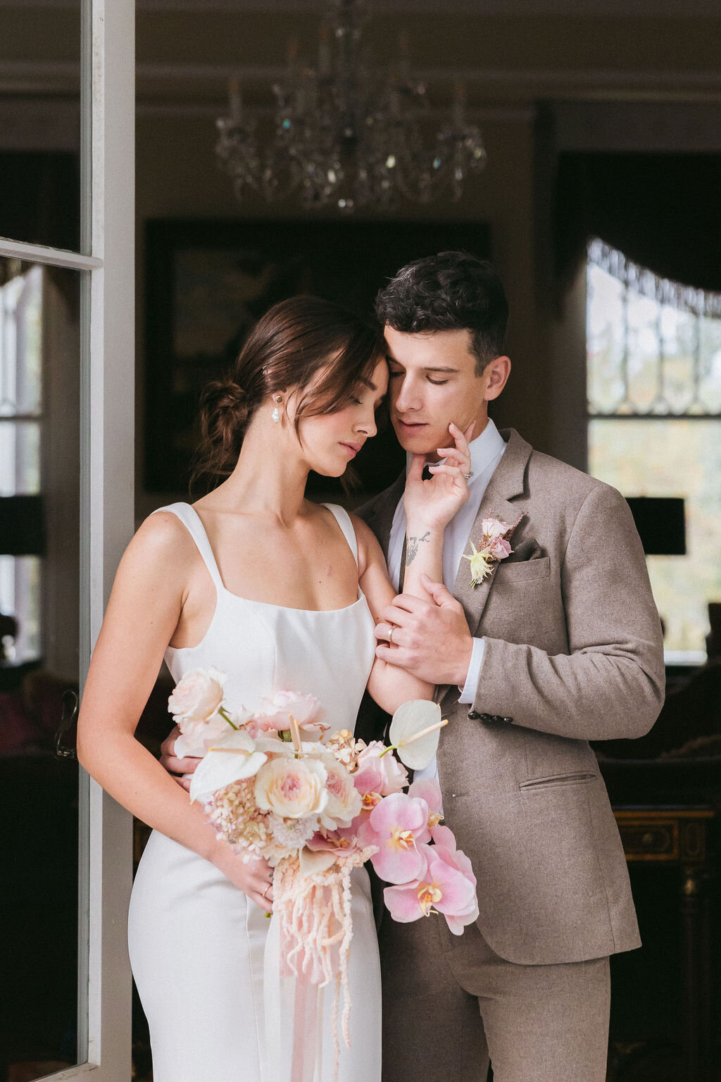 Bride with a pastel orchid bouquet leans into the groom in a doorway at Admiral House, Charleston—captured by luxury wedding photographer Amia Marcell.