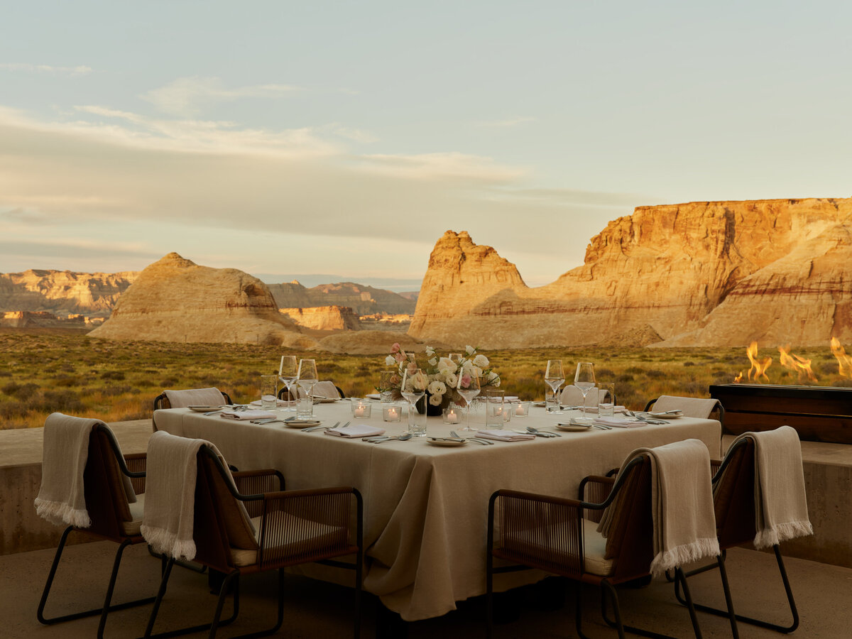 An intimate private dining setup at Amangiri, USA, featuring an elegantly set table with soft linens, floral arrangements, and a backdrop of breathtaking desert mesas at sunset.