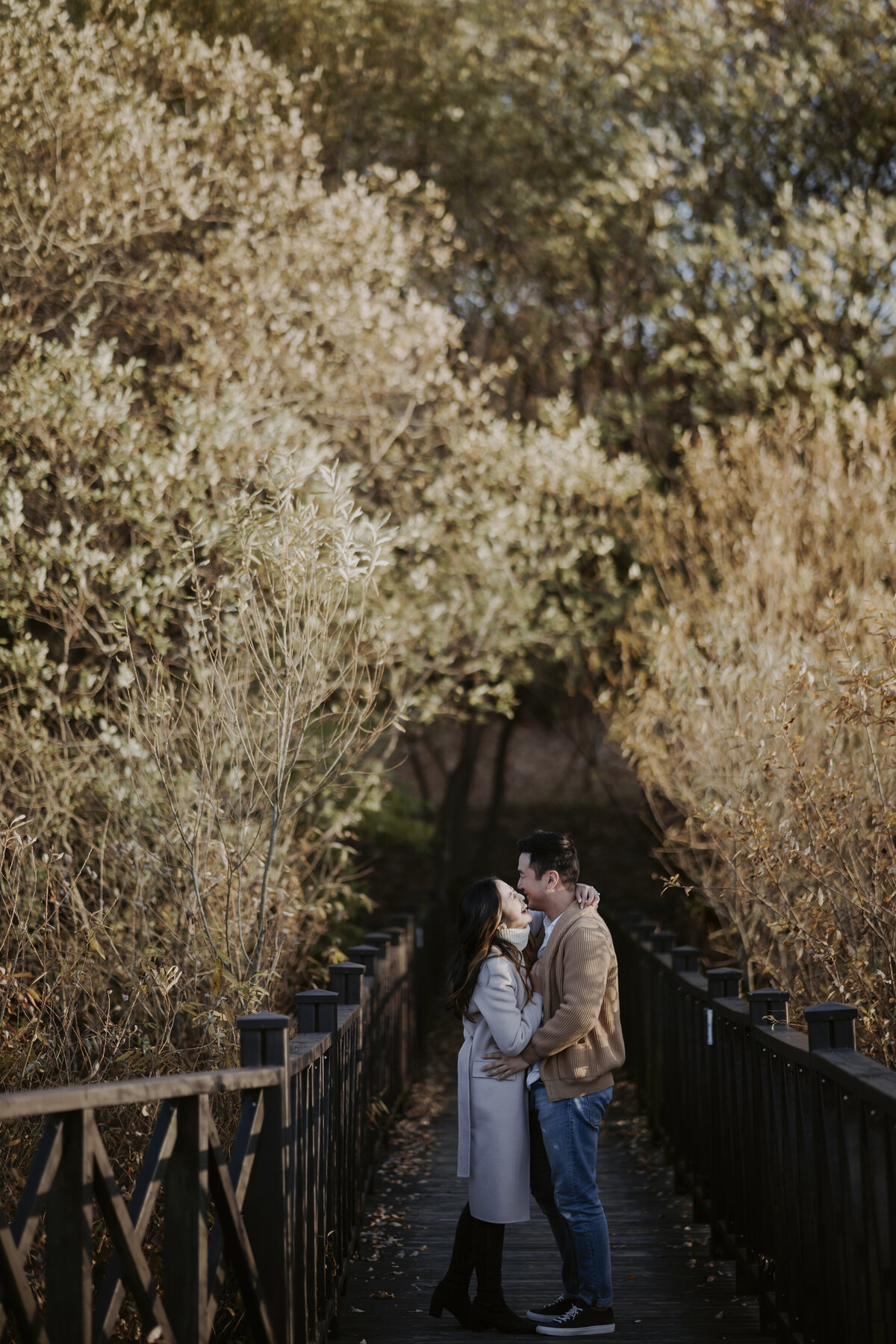 the couple hugging and laughing while standing in a bridge in damyang eco park