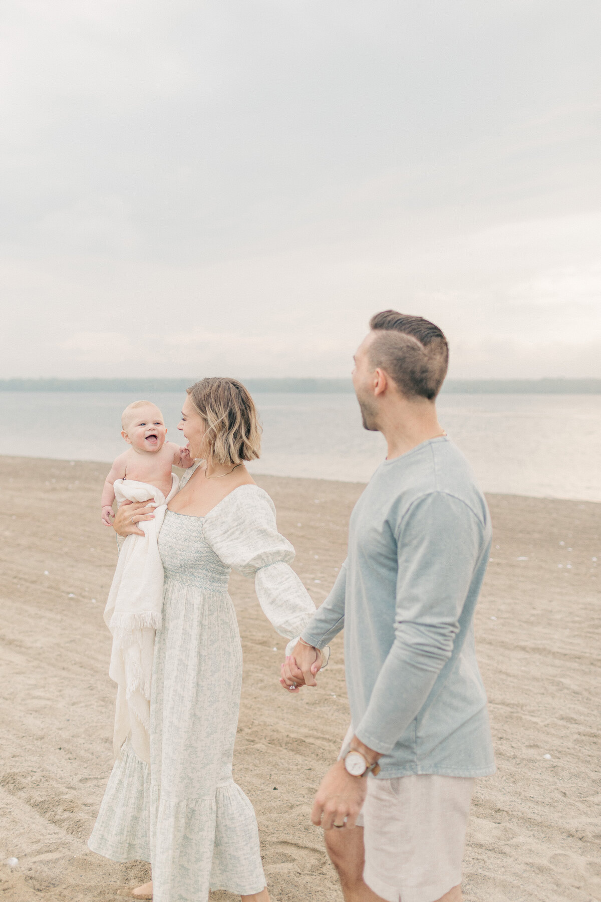 Parents walking hand-in-hand with their baby boy on the sandy shore of a Kansas City lake.