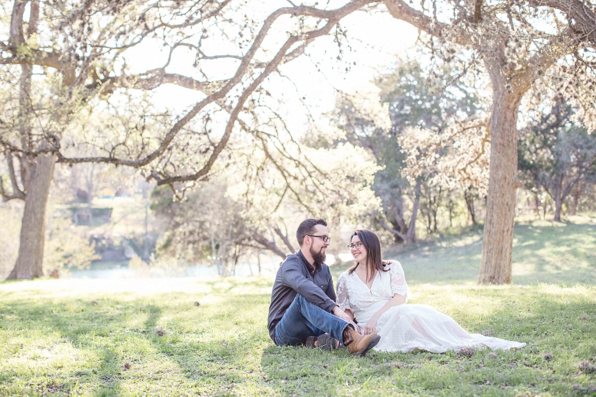 light and airy trees  couple sitting in grass  by Austin wedding photographer Firefly Photography