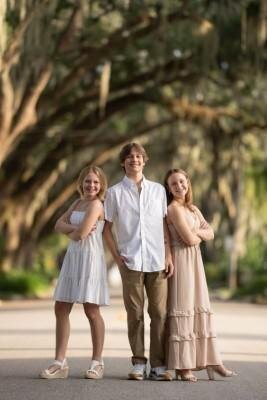 Three siblings posing together on tree-lined path during professional family photo session by St Augustine family photographers