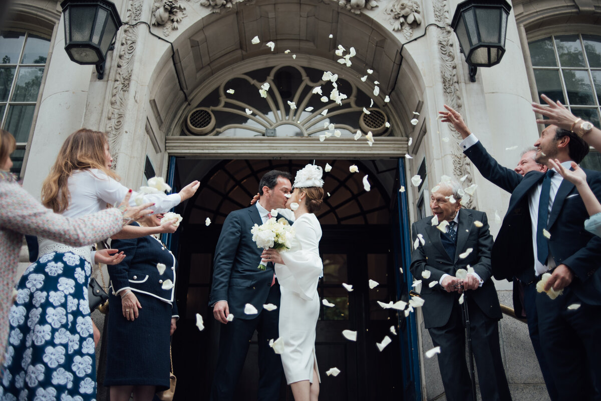 A newly married couple sharing a kiss whilst wedding guests throw confetti at them taken by London Wedding Photographer Liberty Pearl