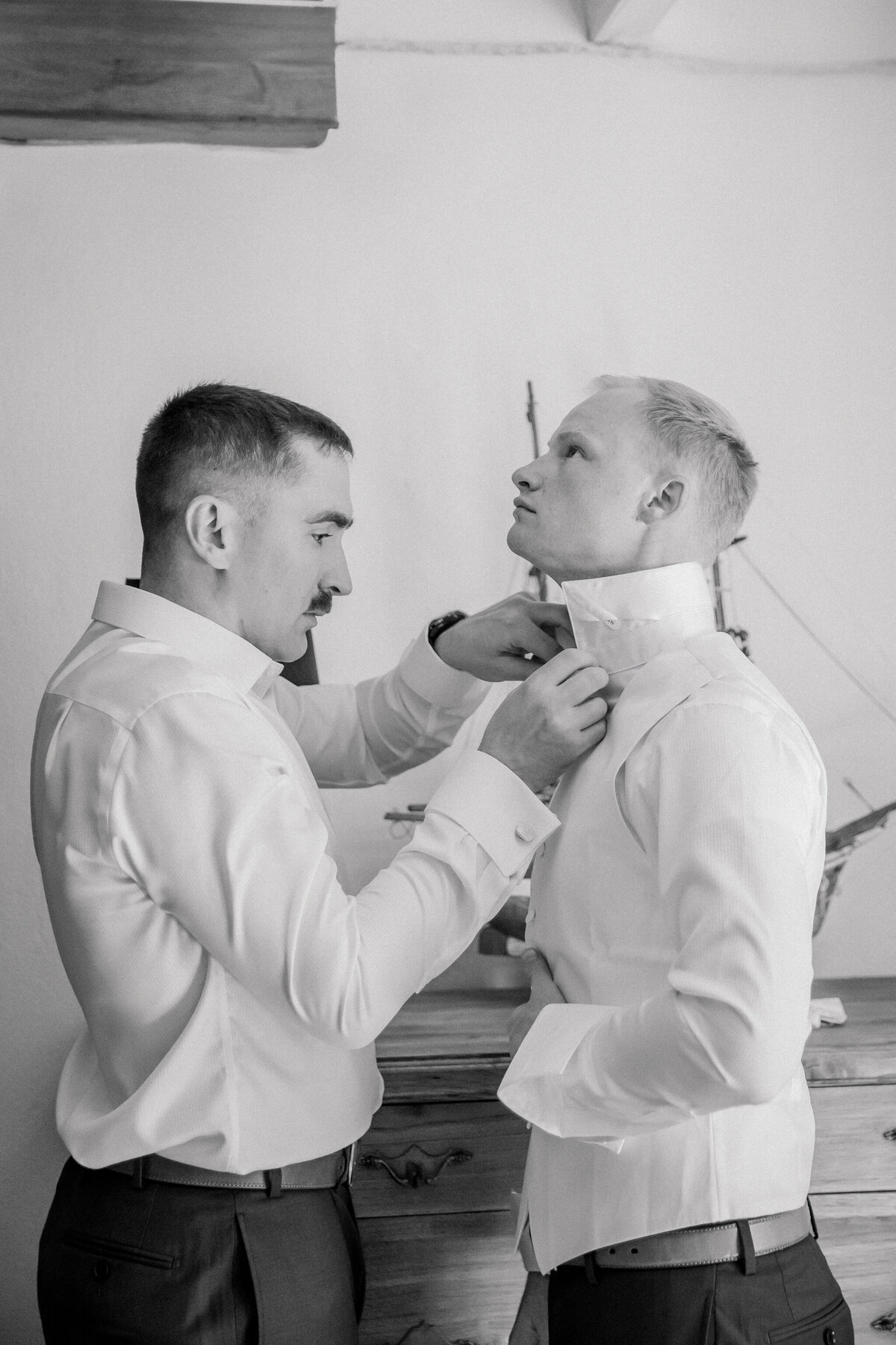 Destination Wedding in Spain | Black and White image of best man helping groom tie his bow tie before his wedding in Spain. Captured by Luxury Destination Photographer, Caitlin Wilcox.