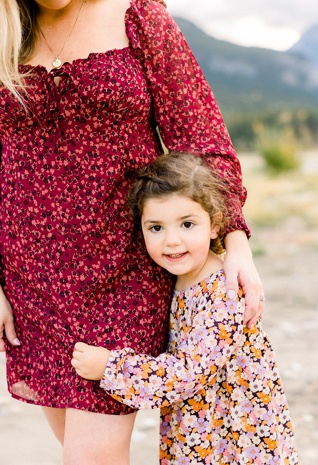 Young girl clinging to mom while smiling in a floral dress