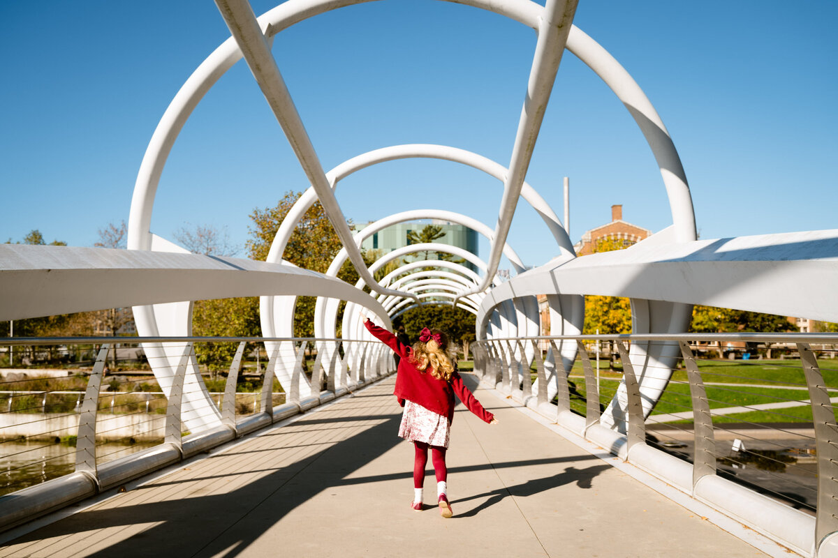 A small child running across an industrial bridge with their arms outstretched.