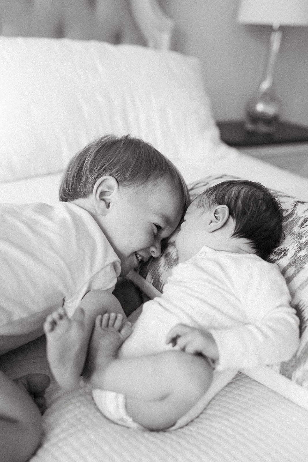 Older brother lying on a pillow, touching noses with his newborn sibling during an in-home newborn session